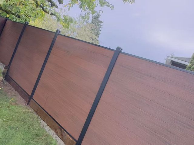 Walnut composite fence with black aluminum posts along a garden path